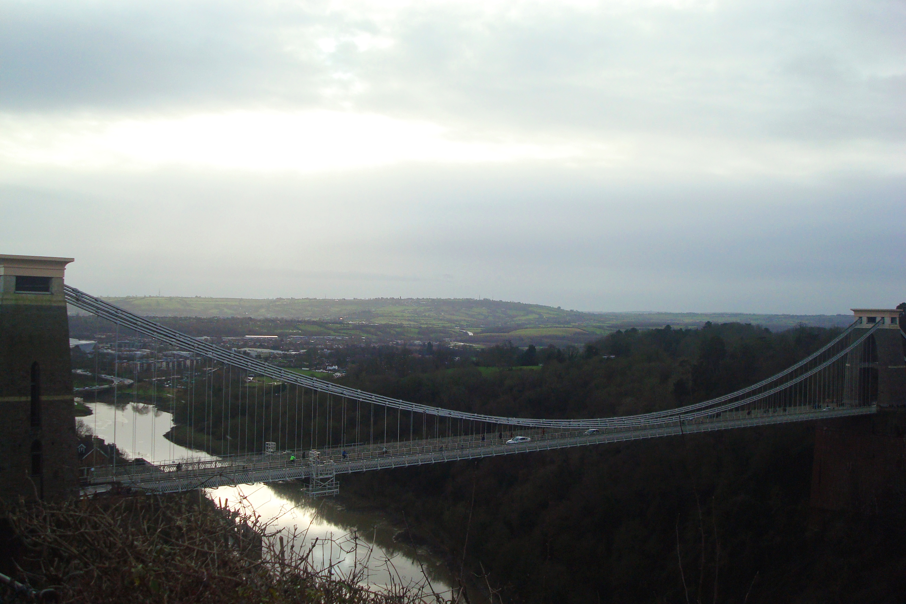 Een natuurfoto vanuit het vogelperspectief van de Clifton Suspension Bridge in Bristol, Engeland. Het is een bewolkte dag en het oogt donker en grijs.
