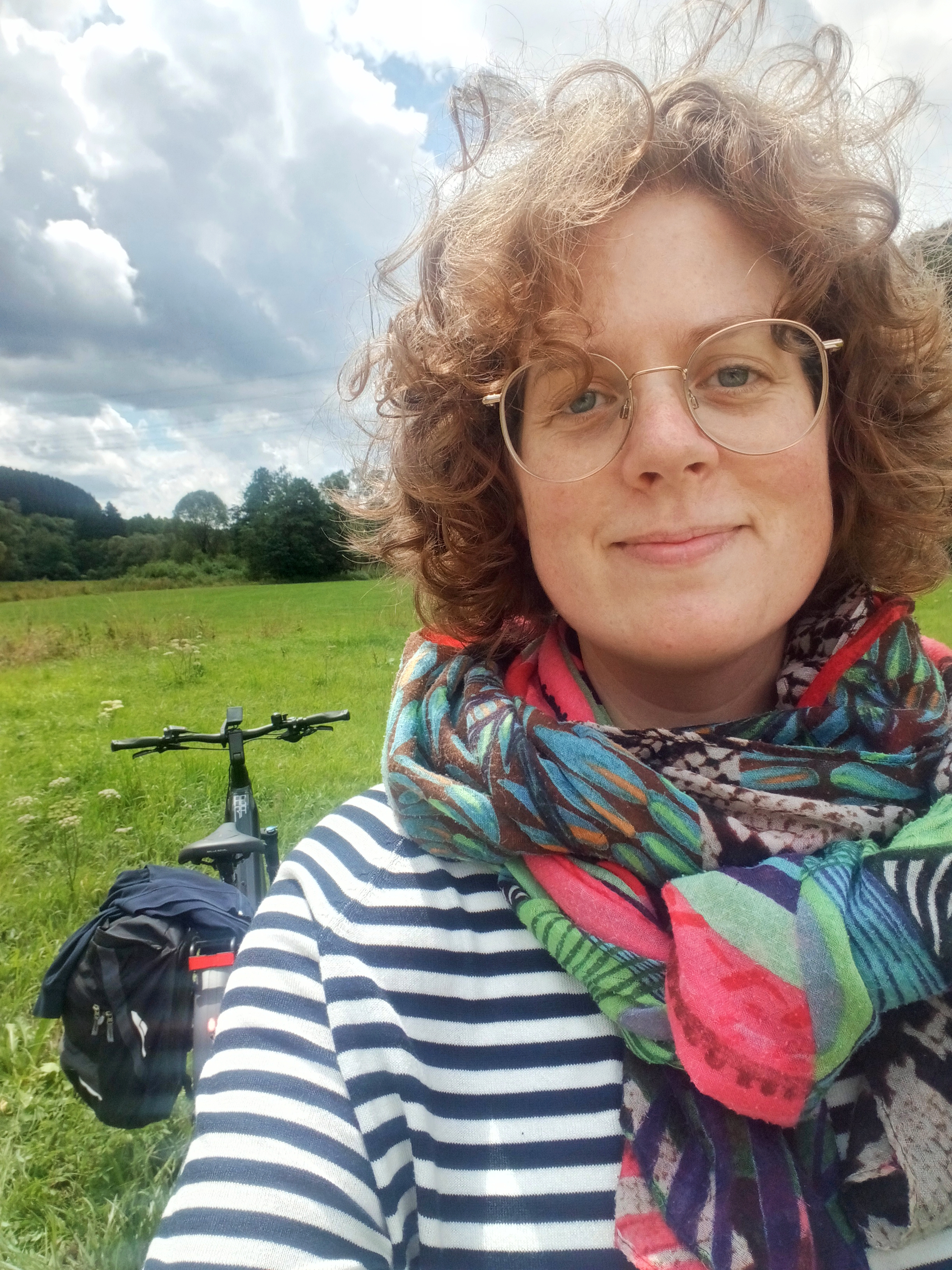Zelfportret met op de achtergrond een fiets, groen grasveld en blauwe lucht met wolken.
