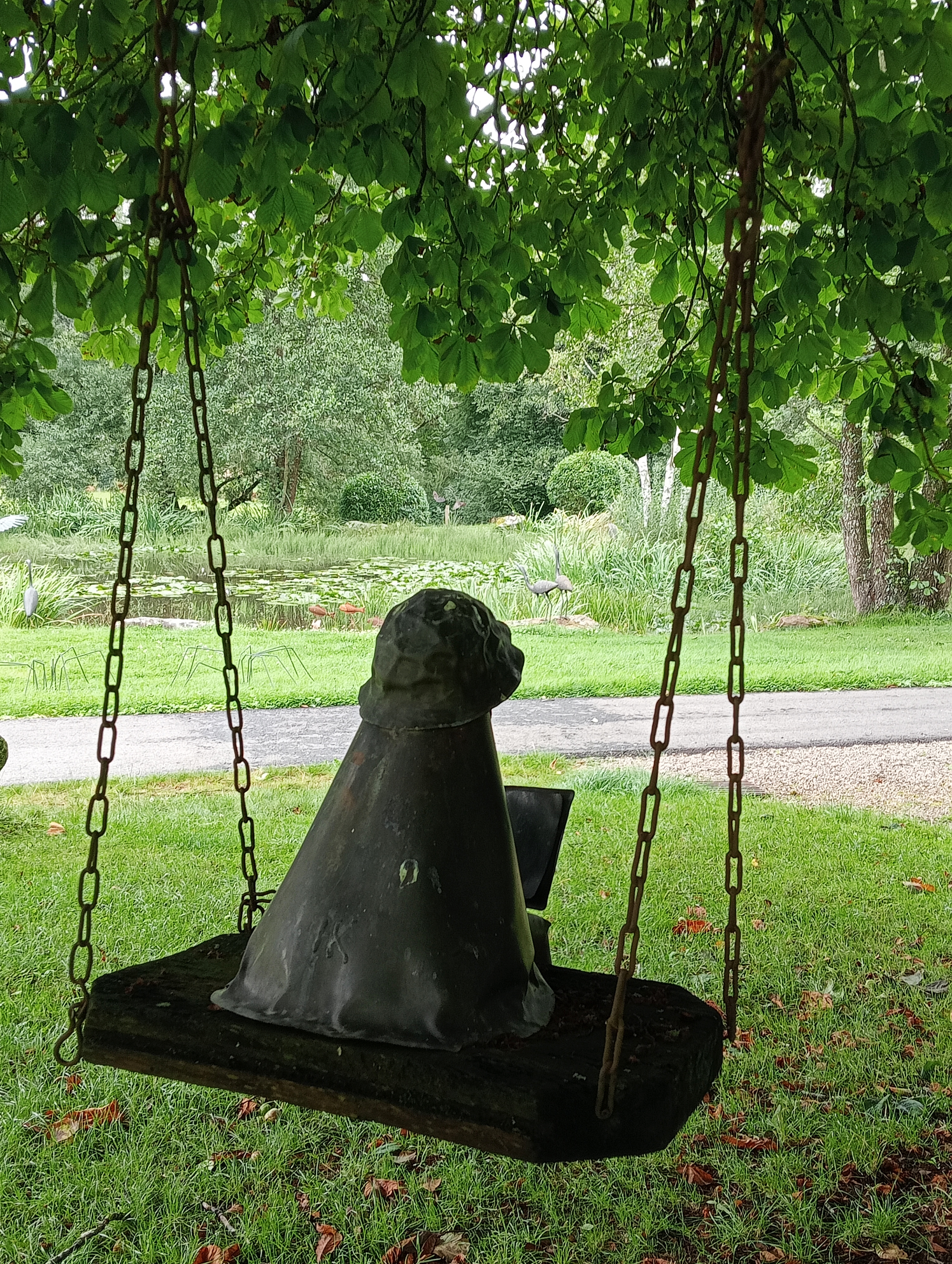 Foto van een koperen beeld, meisje lezend op de schommel in een boom. Skulpturenpark Krüft - Niederprüm