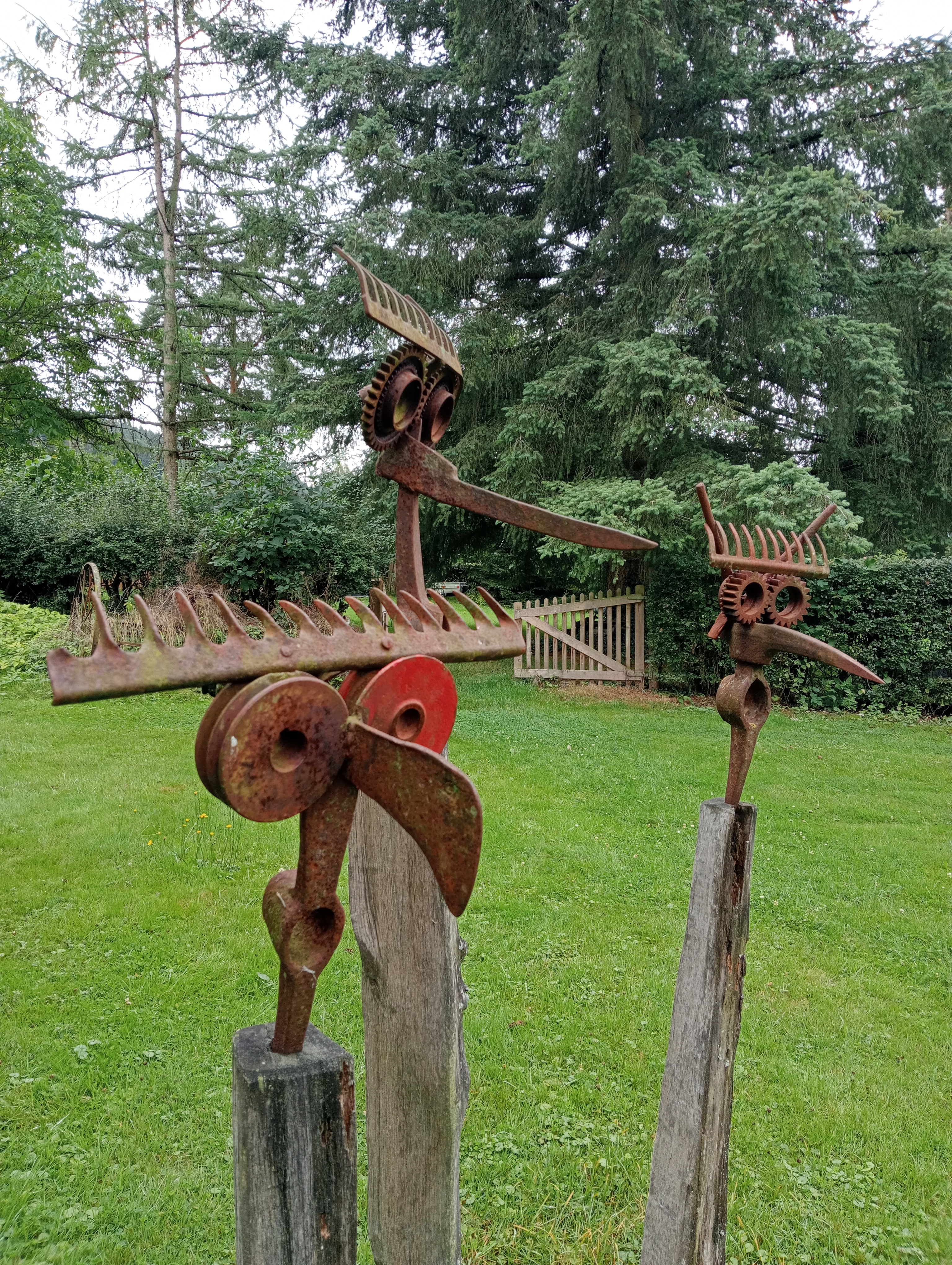 Een foto van drie beelden in de Skulpturenpark Kruft. Gezichten gemaakt van een hark, bijl en houweel.