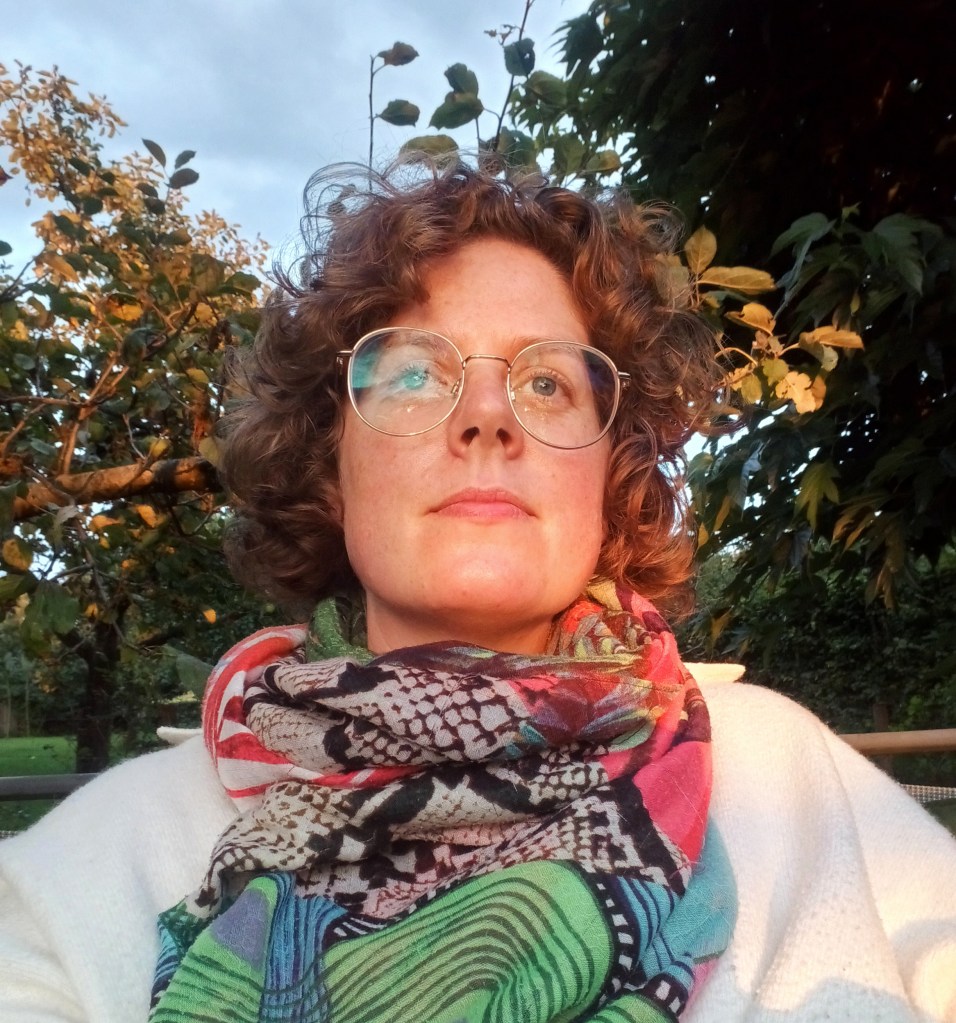Een foto van mezelf, met bril en gekleurde sjaal. Op mijn gezicht de gloed van de avondzon.